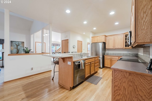 kitchen featuring a kitchen island with sink, sink, light hardwood / wood-style flooring, appliances with stainless steel finishes, and a breakfast bar area