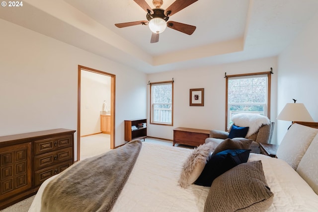 bedroom featuring a tray ceiling, ensuite bath, ceiling fan, and light carpet