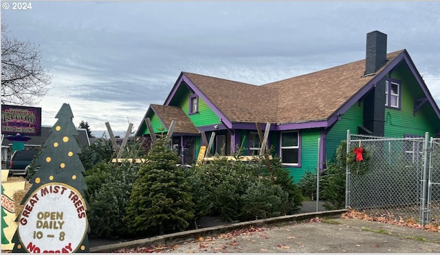 view of front of property with a shingled roof, a chimney, and fence