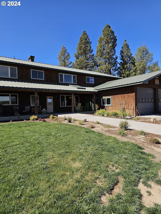 view of front of home with a chimney, covered porch, an attached garage, a front yard, and metal roof