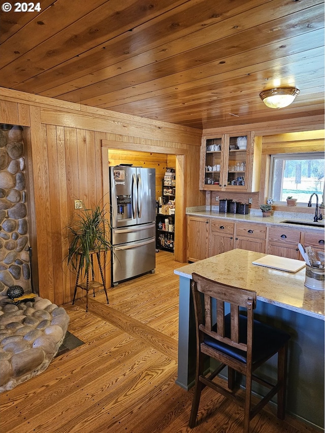 kitchen with stainless steel refrigerator with ice dispenser, light hardwood / wood-style flooring, sink, wood ceiling, and wood walls