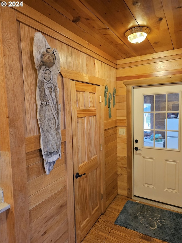 doorway with light wood finished floors, wood ceiling, and wooden walls