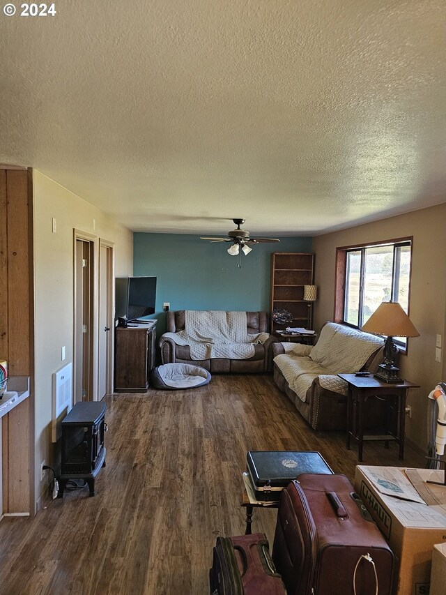 living room featuring a wood stove, a textured ceiling, dark hardwood / wood-style floors, and ceiling fan