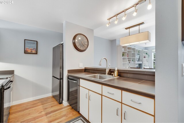 kitchen with white cabinets, light wood-type flooring, pendant lighting, sink, and appliances with stainless steel finishes