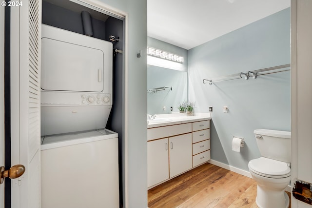 bathroom with stacked washer and clothes dryer, vanity, hardwood / wood-style flooring, and toilet