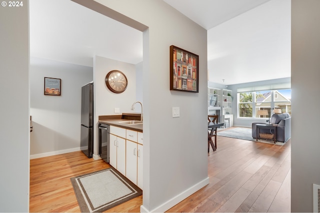 interior space featuring black refrigerator, white cabinetry, dishwasher, sink, and light hardwood / wood-style floors