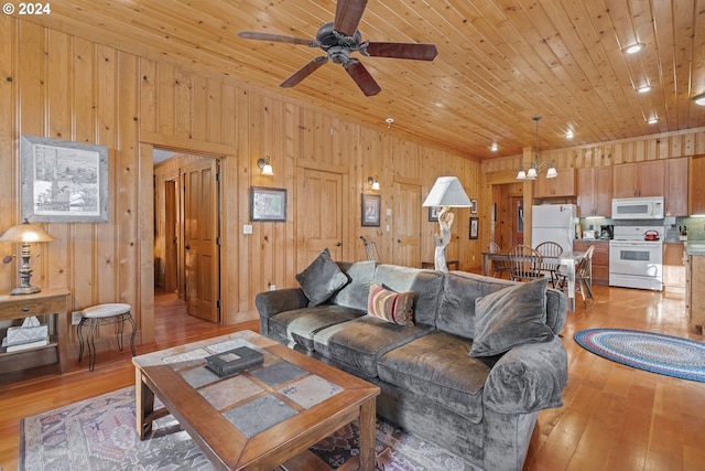 living room featuring ceiling fan with notable chandelier, light hardwood / wood-style floors, and wooden walls