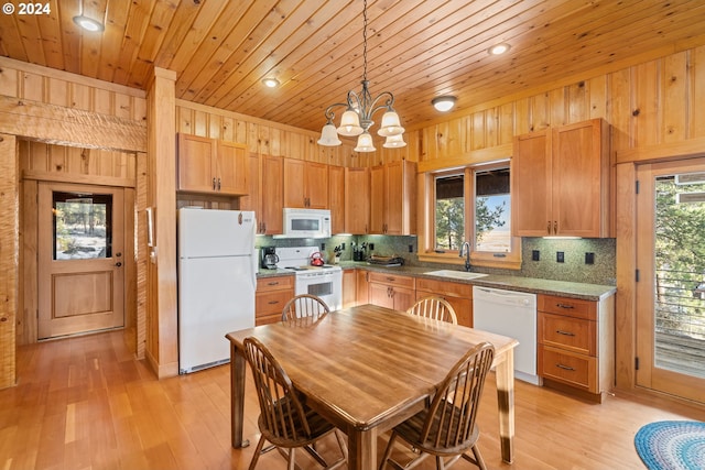 kitchen with wood walls, white appliances, hanging light fixtures, and light hardwood / wood-style flooring