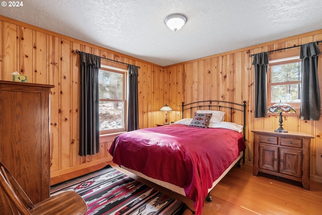 bedroom featuring a textured ceiling, wooden walls, and light hardwood / wood-style flooring