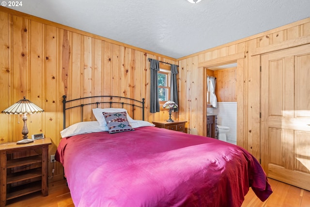 bedroom featuring a textured ceiling, light wood-type flooring, wooden walls, and connected bathroom