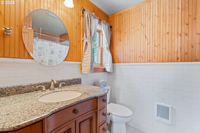 bathroom featuring heating unit, a textured ceiling, toilet, vanity, and tile walls