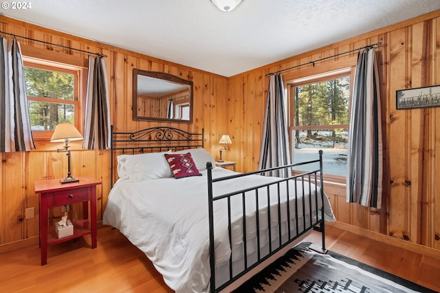 bedroom with hardwood / wood-style floors, a textured ceiling, multiple windows, and wooden walls