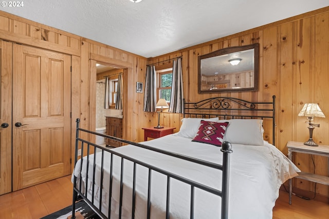 bedroom featuring wooden walls, light hardwood / wood-style floors, and a textured ceiling