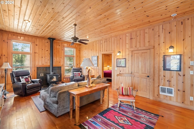 living room with ceiling fan, wooden walls, hardwood / wood-style flooring, wooden ceiling, and a wood stove