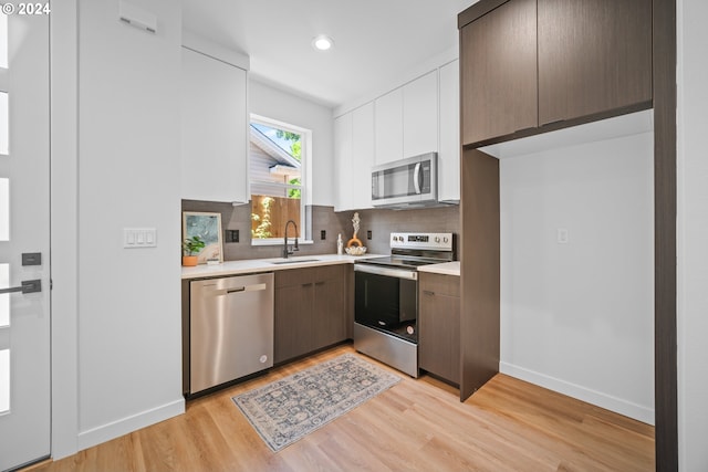 kitchen featuring decorative backsplash, appliances with stainless steel finishes, light wood-type flooring, sink, and white cabinetry