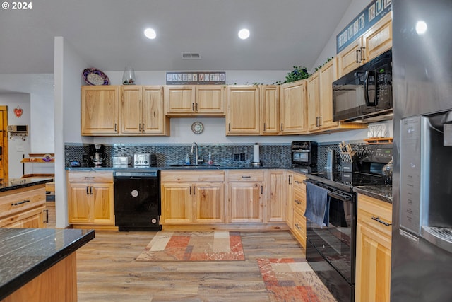 kitchen with sink, light brown cabinets, light hardwood / wood-style flooring, dark stone counters, and black appliances