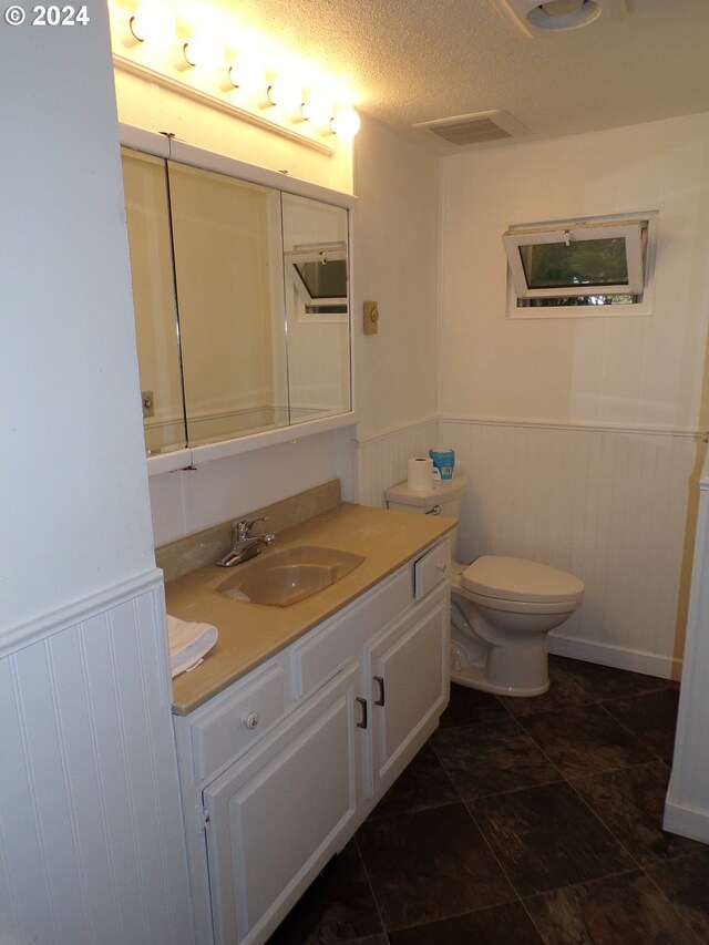 bathroom with a textured ceiling, vanity, tile patterned flooring, toilet, and wood walls