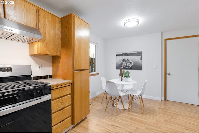 kitchen featuring stainless steel gas stove, a textured ceiling, light wood-type flooring, and wall chimney exhaust hood