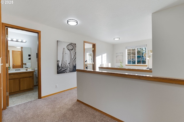 corridor featuring light colored carpet, a textured ceiling, and sink