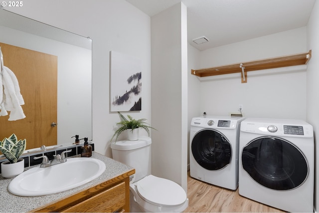 clothes washing area featuring independent washer and dryer, light wood-type flooring, and sink