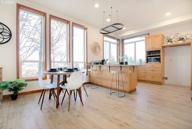 kitchen featuring light hardwood / wood-style floors, a breakfast bar area, a healthy amount of sunlight, light brown cabinetry, and oven