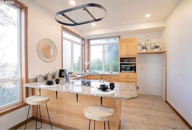 kitchen with a breakfast bar, kitchen peninsula, built in microwave, light brown cabinets, and light stone counters