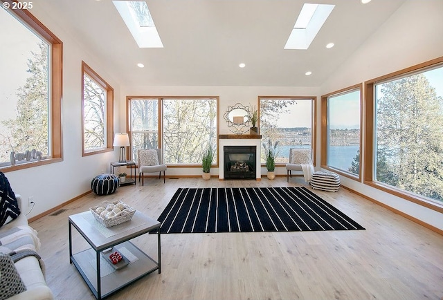 living room featuring vaulted ceiling with skylight, light hardwood / wood-style flooring, and a water view