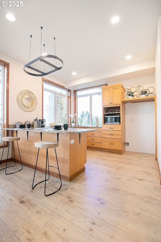 kitchen featuring light hardwood / wood-style floors, light brown cabinets, wall oven, and a breakfast bar area