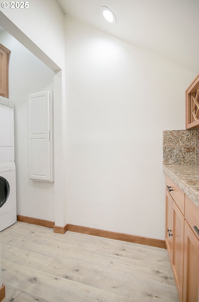 washroom featuring cabinets, stacked washing maching and dryer, and light hardwood / wood-style floors