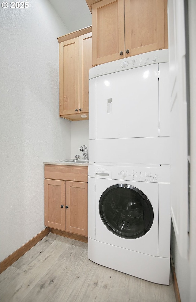 laundry room featuring cabinets, stacked washer / drying machine, light hardwood / wood-style flooring, and sink