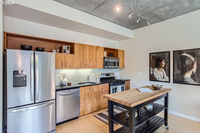 kitchen with tasteful backsplash, stainless steel appliances, sink, rail lighting, and light wood-type flooring