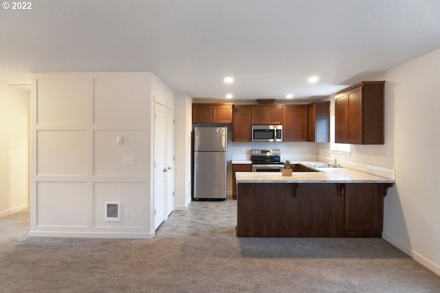 kitchen with kitchen peninsula, appliances with stainless steel finishes, a kitchen breakfast bar, light colored carpet, and sink