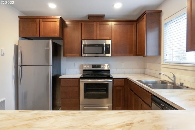 kitchen with appliances with stainless steel finishes, a sink, light countertops, recessed lighting, and brown cabinetry