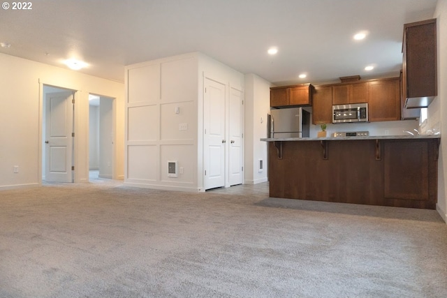 kitchen with appliances with stainless steel finishes, carpet, a kitchen bar, a peninsula, and brown cabinets