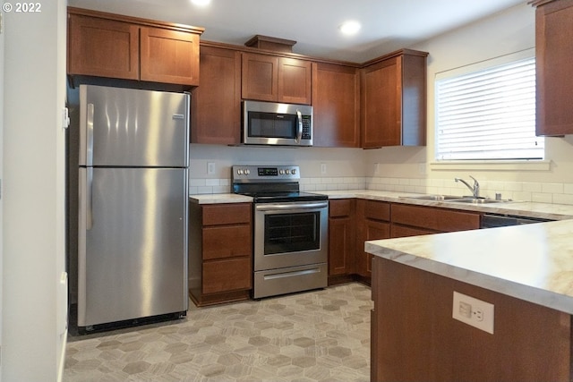 kitchen with stainless steel appliances, a sink, light flooring, light countertops, and brown cabinets