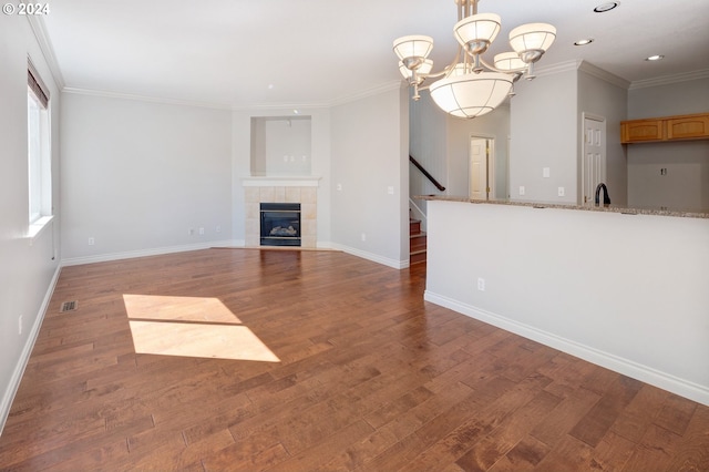 unfurnished living room featuring a fireplace, ornamental molding, an inviting chandelier, and dark wood-type flooring