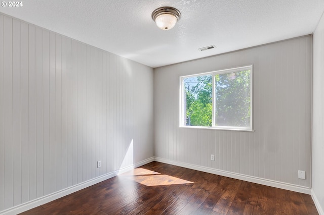 empty room with wood walls, wood-type flooring, and a textured ceiling