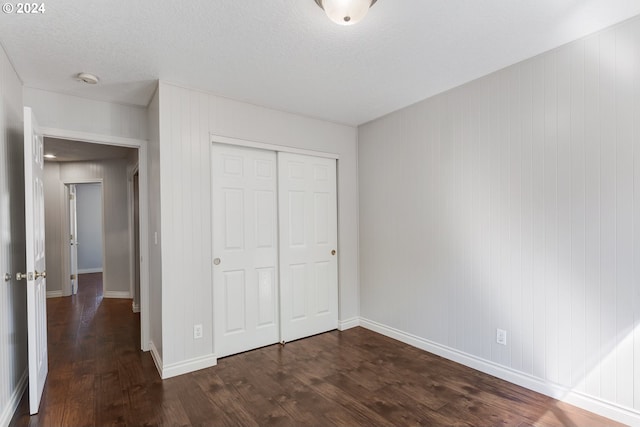 unfurnished bedroom with a textured ceiling, dark hardwood / wood-style floors, a closet, and wood walls