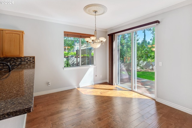 unfurnished dining area featuring hardwood / wood-style floors, a wealth of natural light, crown molding, and a notable chandelier