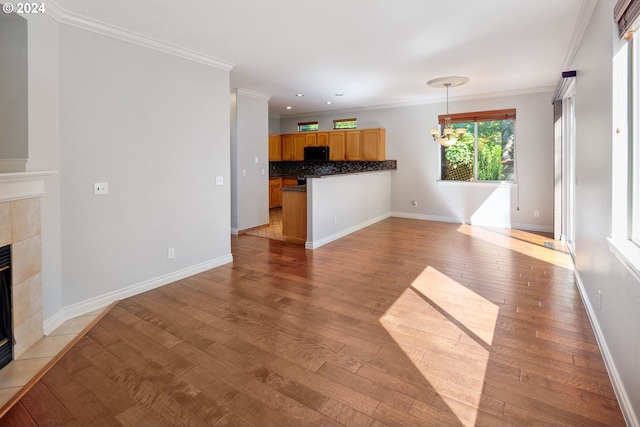 unfurnished living room featuring light hardwood / wood-style flooring, a notable chandelier, ornamental molding, and a tiled fireplace