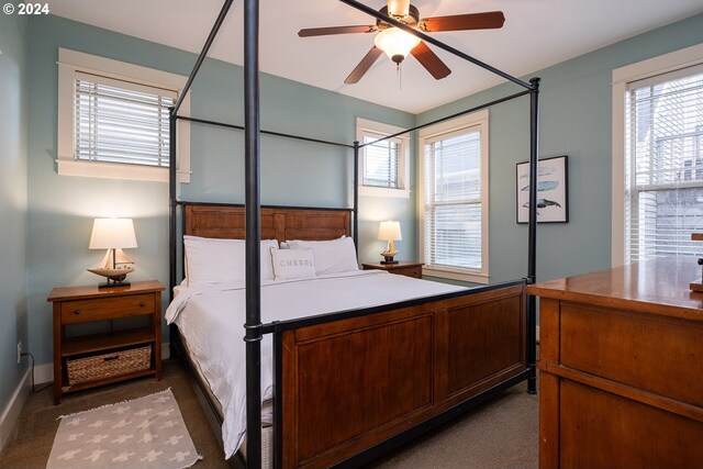 bedroom featuring ceiling fan, dark carpet, and multiple windows