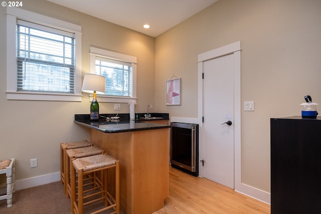 bar featuring wet bar, a sink, light wood-type flooring, beverage cooler, and baseboards