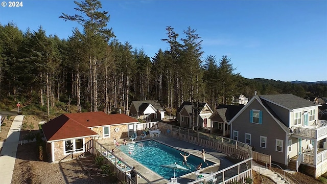 community pool with a wooded view, an outdoor structure, and fence