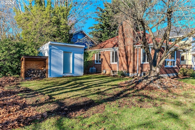 rear view of house with a lawn, central AC unit, and a storage shed