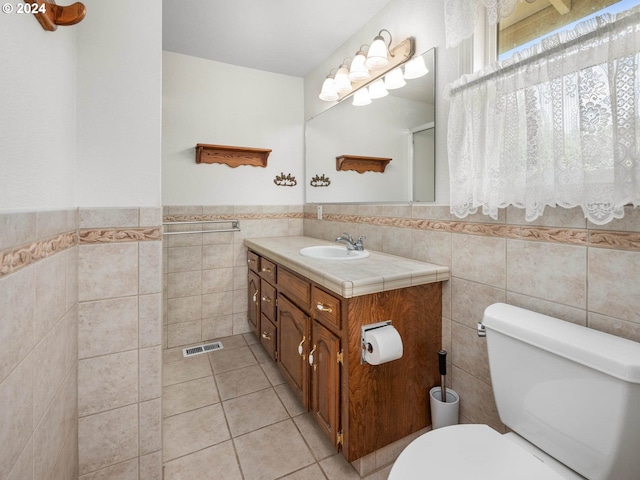 bathroom featuring tile patterned flooring, vanity, toilet, and tile walls