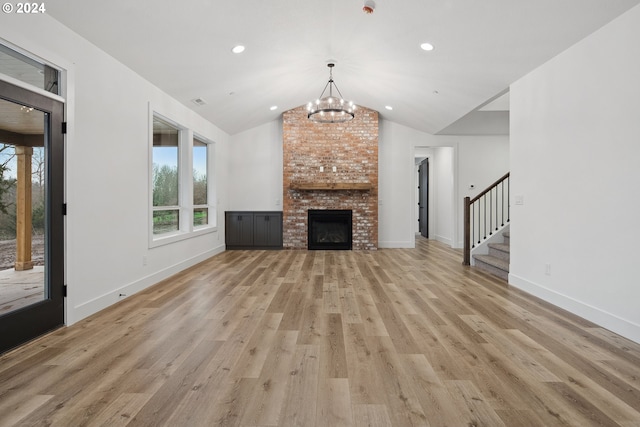 unfurnished living room with a notable chandelier, vaulted ceiling, light wood-type flooring, and a brick fireplace