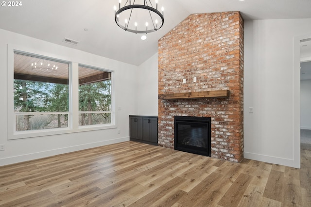 unfurnished living room with a brick fireplace, a notable chandelier, lofted ceiling, and light hardwood / wood-style flooring