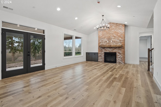 unfurnished living room with lofted ceiling, an inviting chandelier, french doors, a brick fireplace, and light wood-type flooring