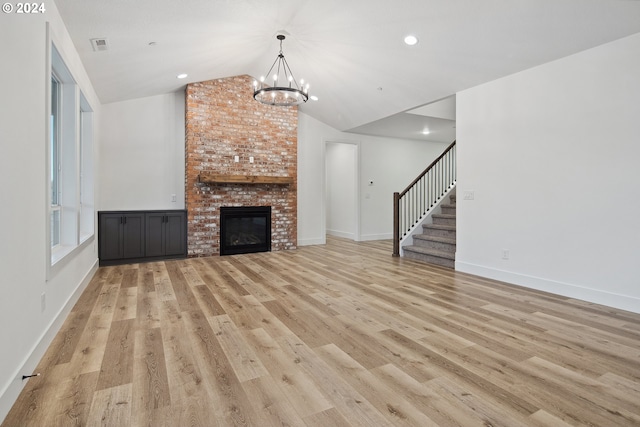 unfurnished living room featuring a fireplace, vaulted ceiling, light hardwood / wood-style flooring, and a notable chandelier