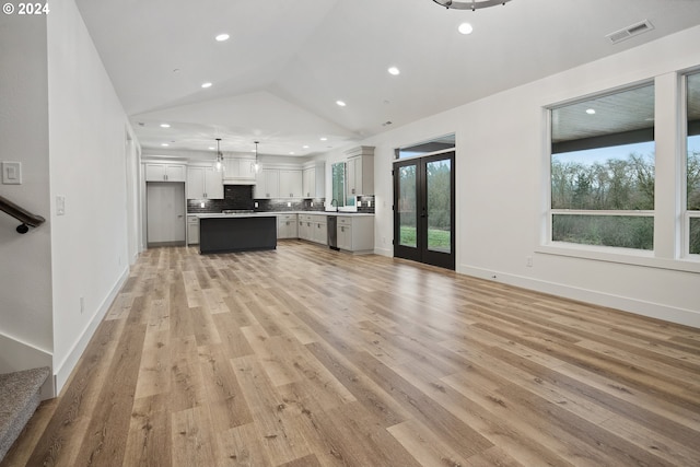 unfurnished living room with sink, french doors, vaulted ceiling, and light wood-type flooring